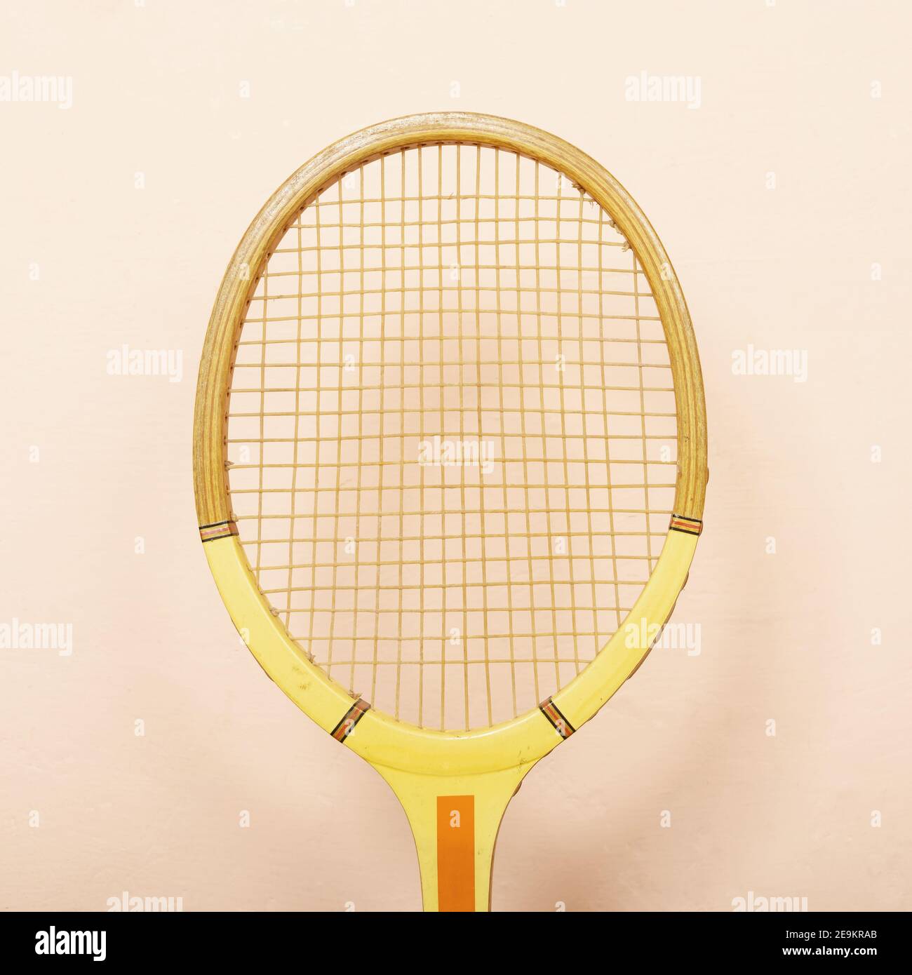 Vintage wooden tennis racket against pink wall, pastel tones of yellow, orange and pink, retro sport concept Stock Photo