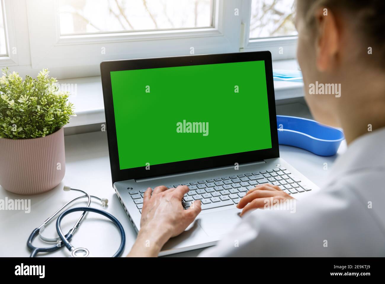 female doctor typing on her laptop computer in medical clinic office. blank green screen mockup Stock Photo