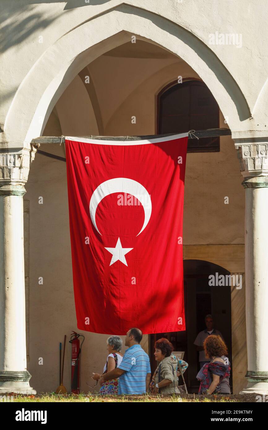 Istanbul, Turkey.  Topkapi Palace. Topkapi Sarayi.  Visitors walking beneath Turkish national flag.  Topkapi is part of the Historic Areas of Istanbul Stock Photo