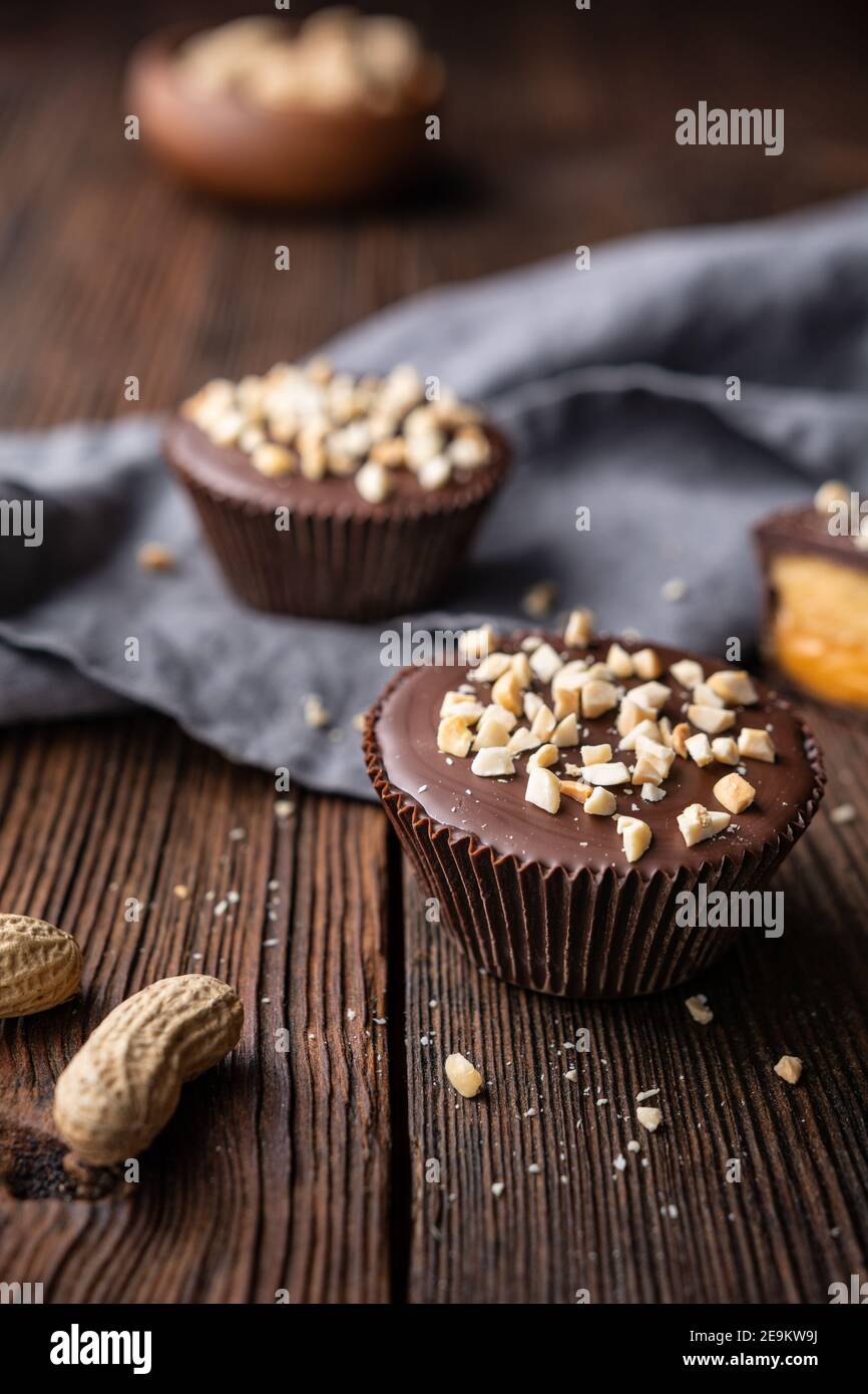 Cold crunchy treat, chocolate cups with caramel and peanut butter filling, sprinkled with chopped nuts on rustic wooden background Stock Photo
