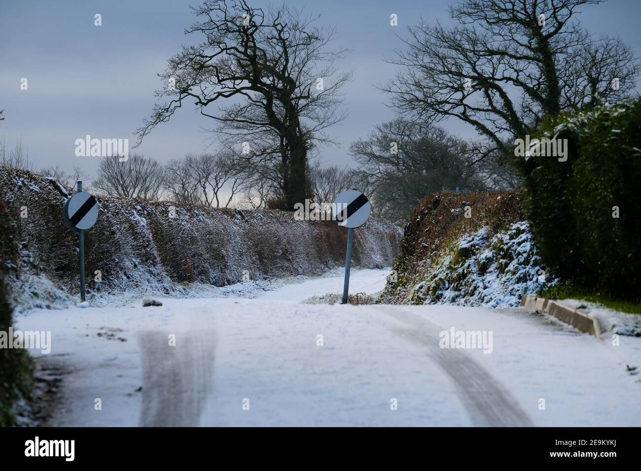Vehicle tracks on snow-covered country lane on the approach  to change of speed limit displays. Stock Photo