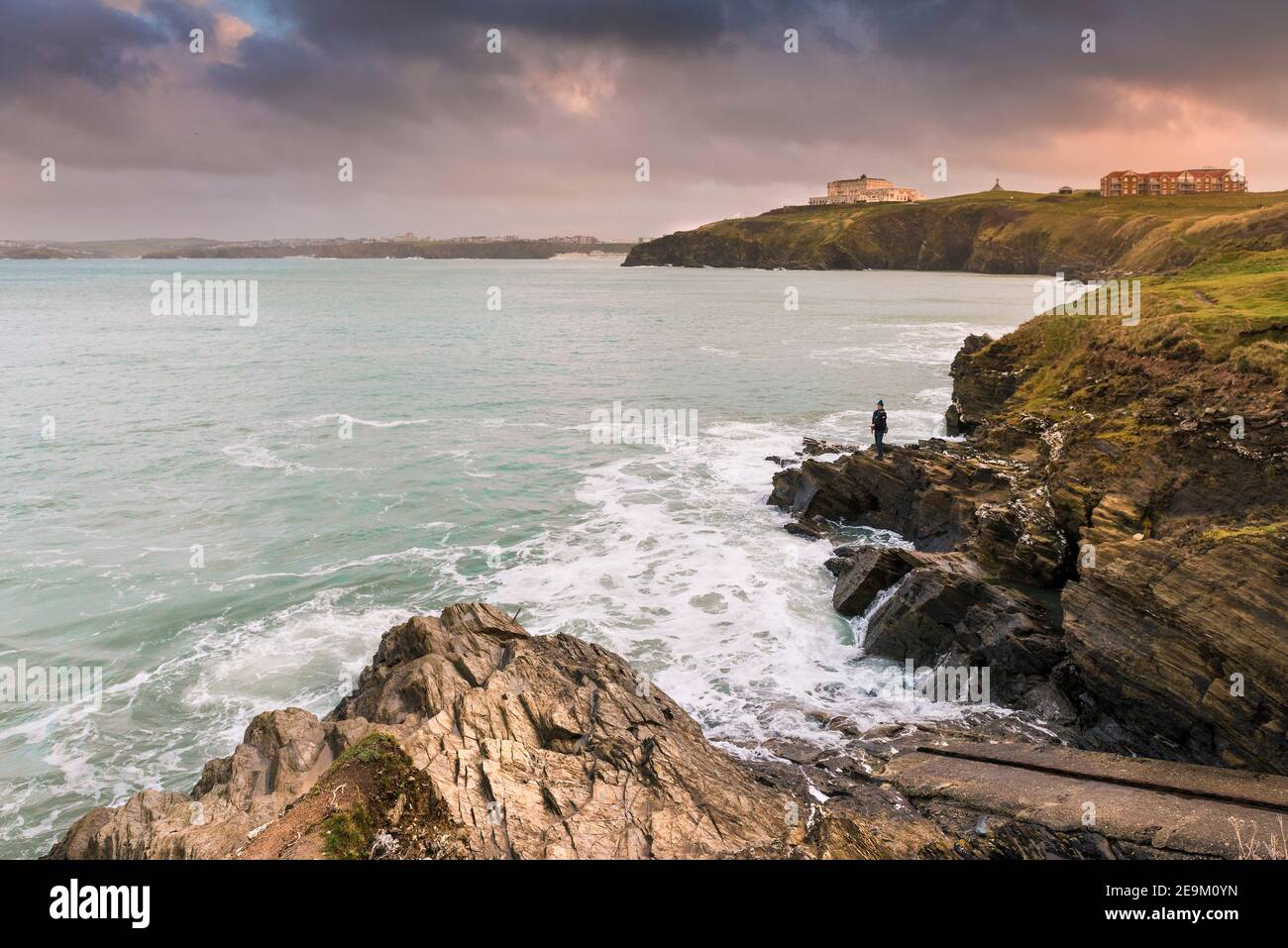 Warm evening light over an angler fishing off rocks on the coastline of Newquay Bay in Cornwall. Stock Photo