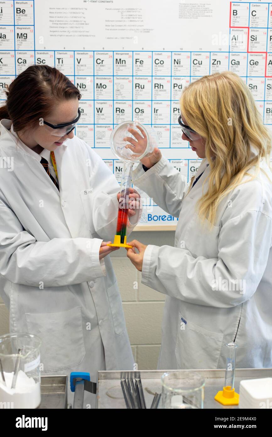 Two teenage female students performing a science experiment with periodic timetable in background. Stock Photo