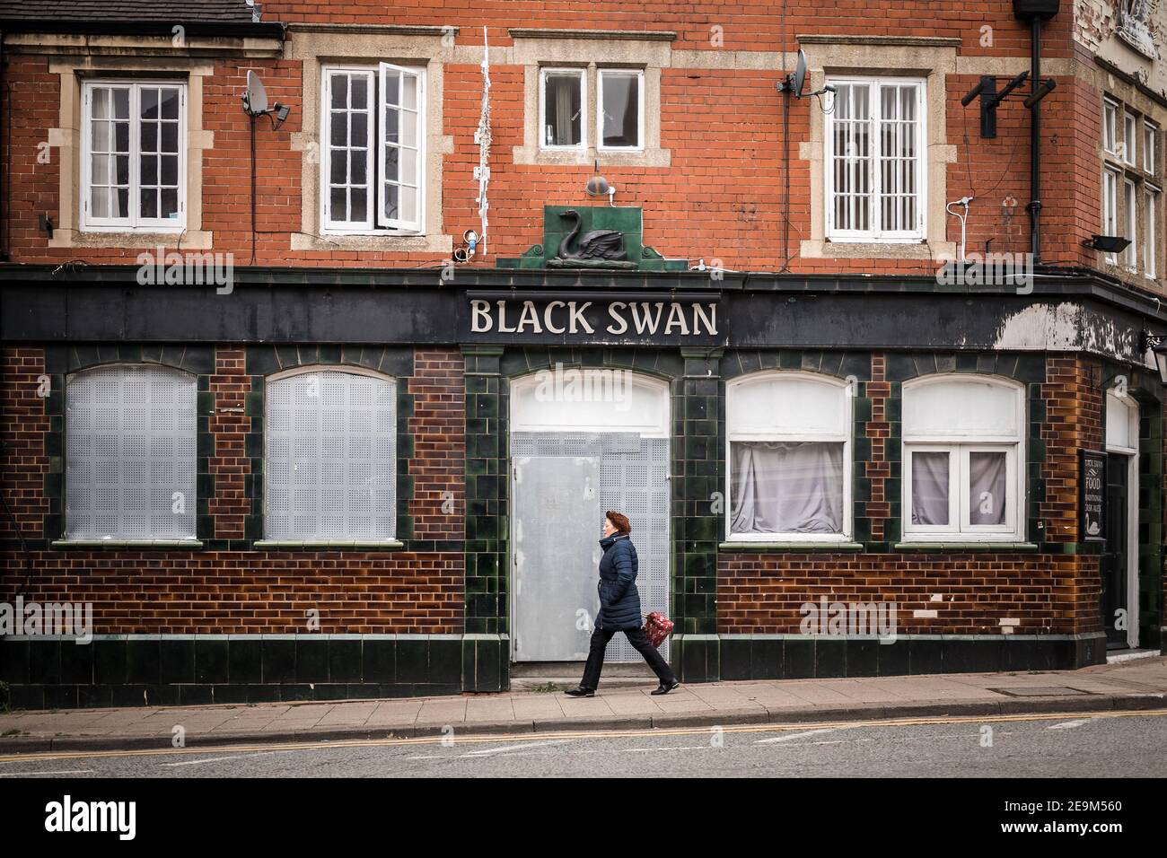 Lone woman walking past closed down boarded up pub public house as town goes into recession and shops close under Covid 19 pandemic lockdown Stock Photo