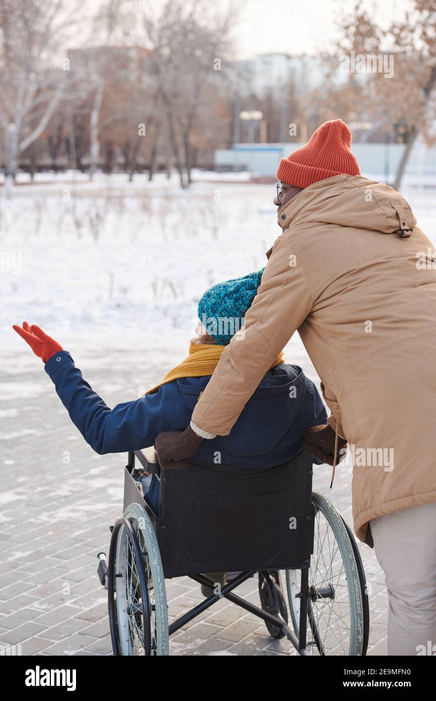 Rear view of disabled woman in wheelchair walking in winter day with ...