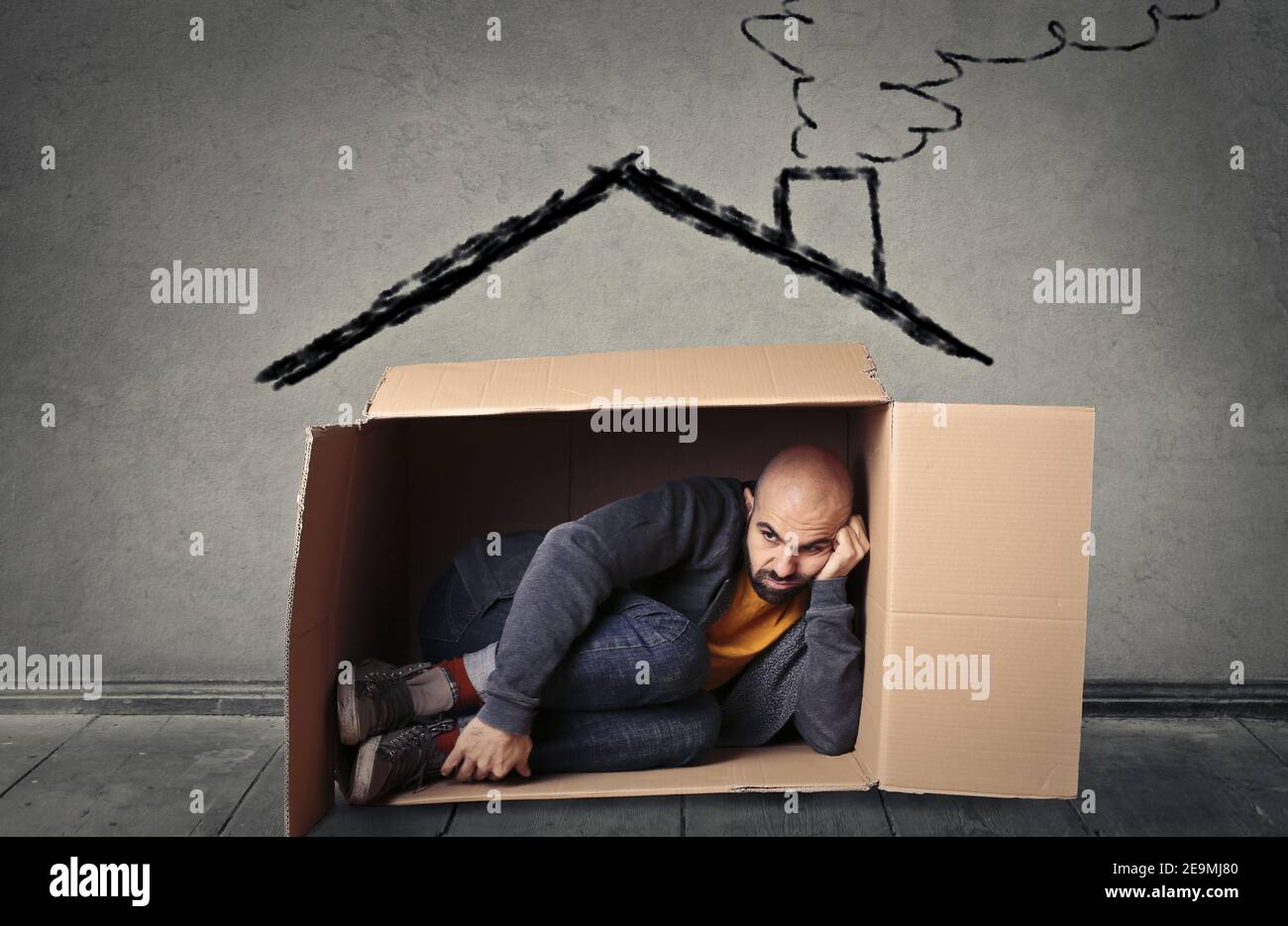 European male sitting in a cardboard box with a house drawn o Stock Photo