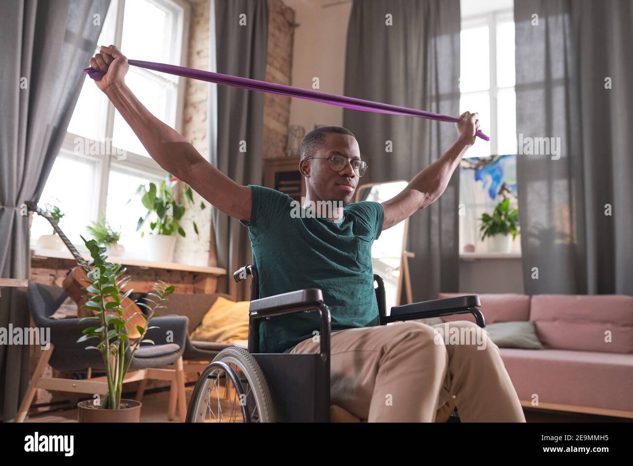 African disabled man sitting in wheelchair raising his arms and doing stretching exercises during sports training at home Stock Photo