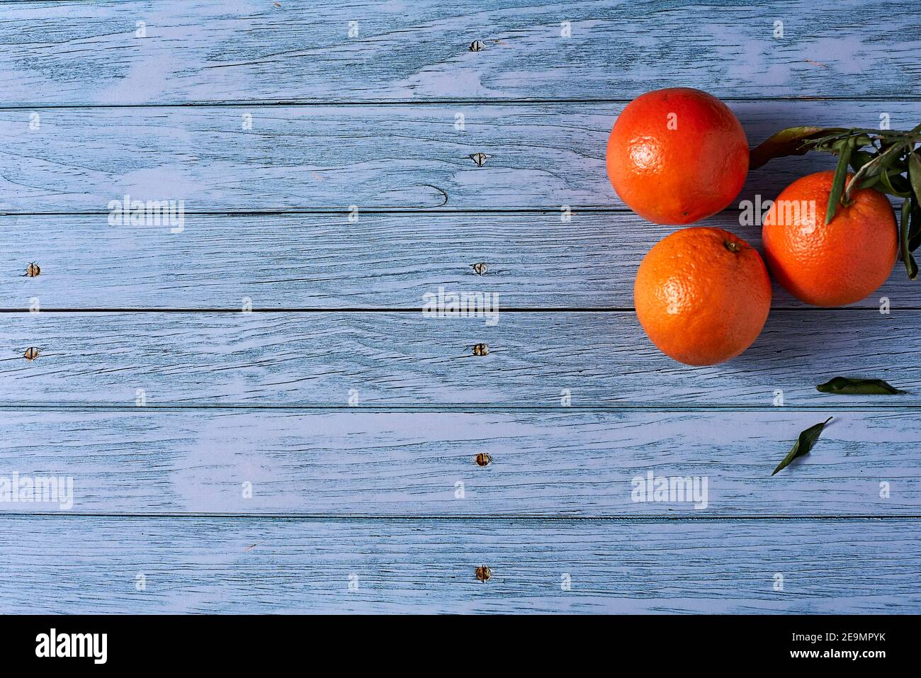 Three oranges on wooden floor with nails, orange leaves, empty space Stock Photo