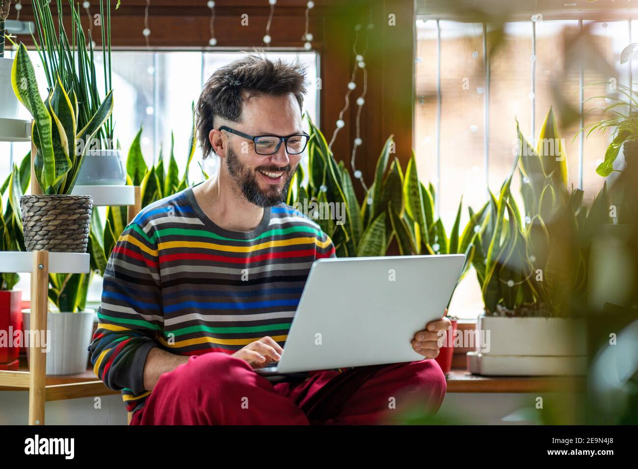 Young man working at home with laptop surrounded by houseplants Stock Photo