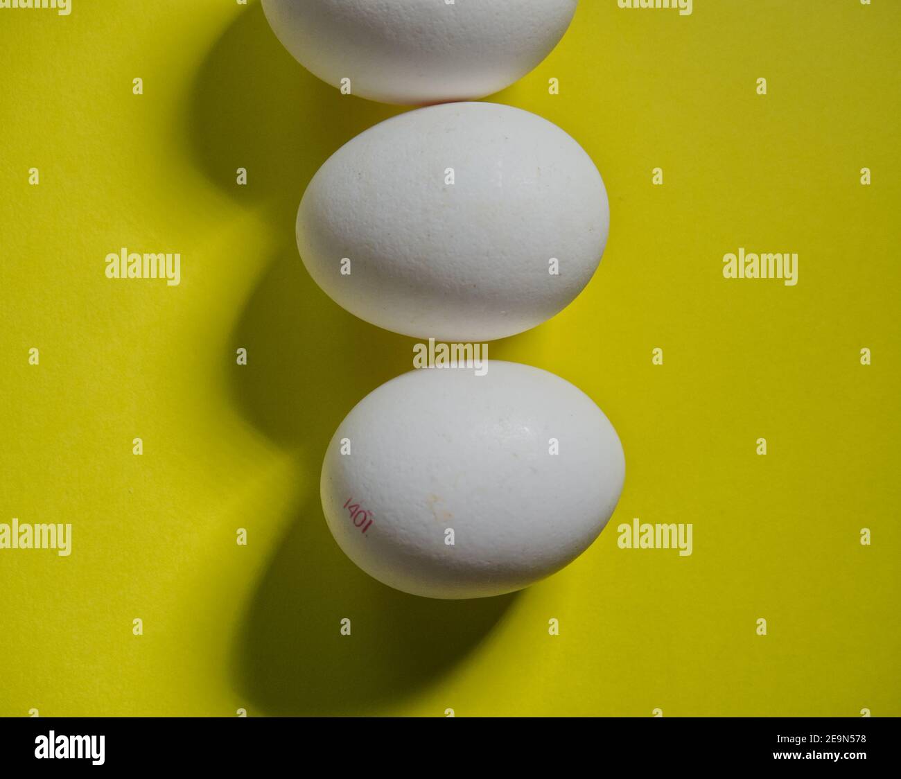 Three white bio eggs on yellow background, topview Stock Photo