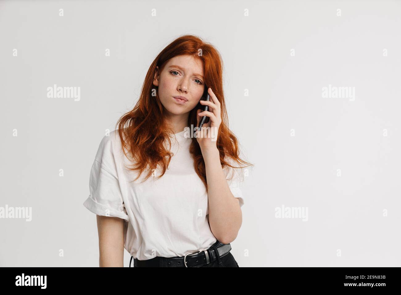Ginger beautiful confused girl talking on cellphone isolated over white ...