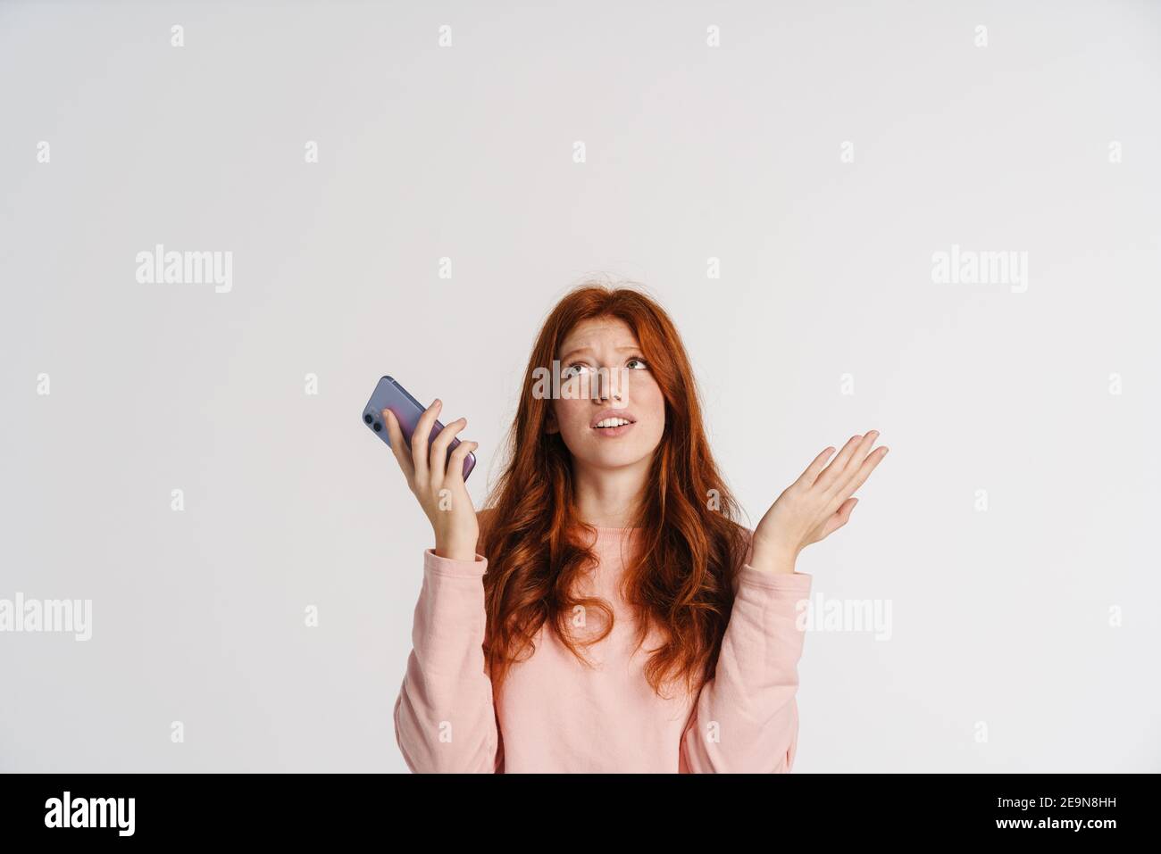 Ginger beautiful unhappy girl holding cellphone and looking upward ...
