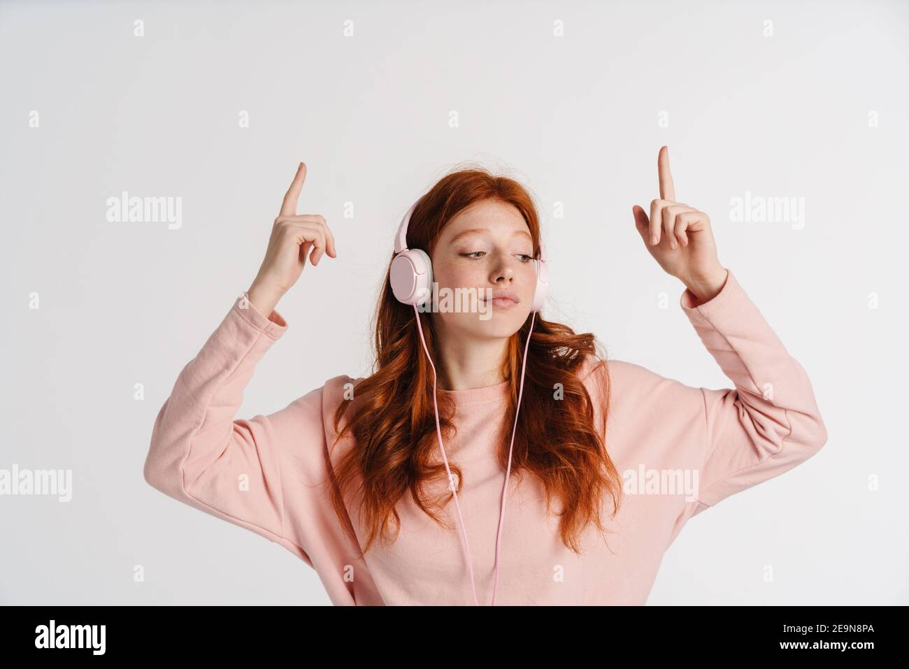Ginger beautiful serious girl in headphones pointing fingers upward ...