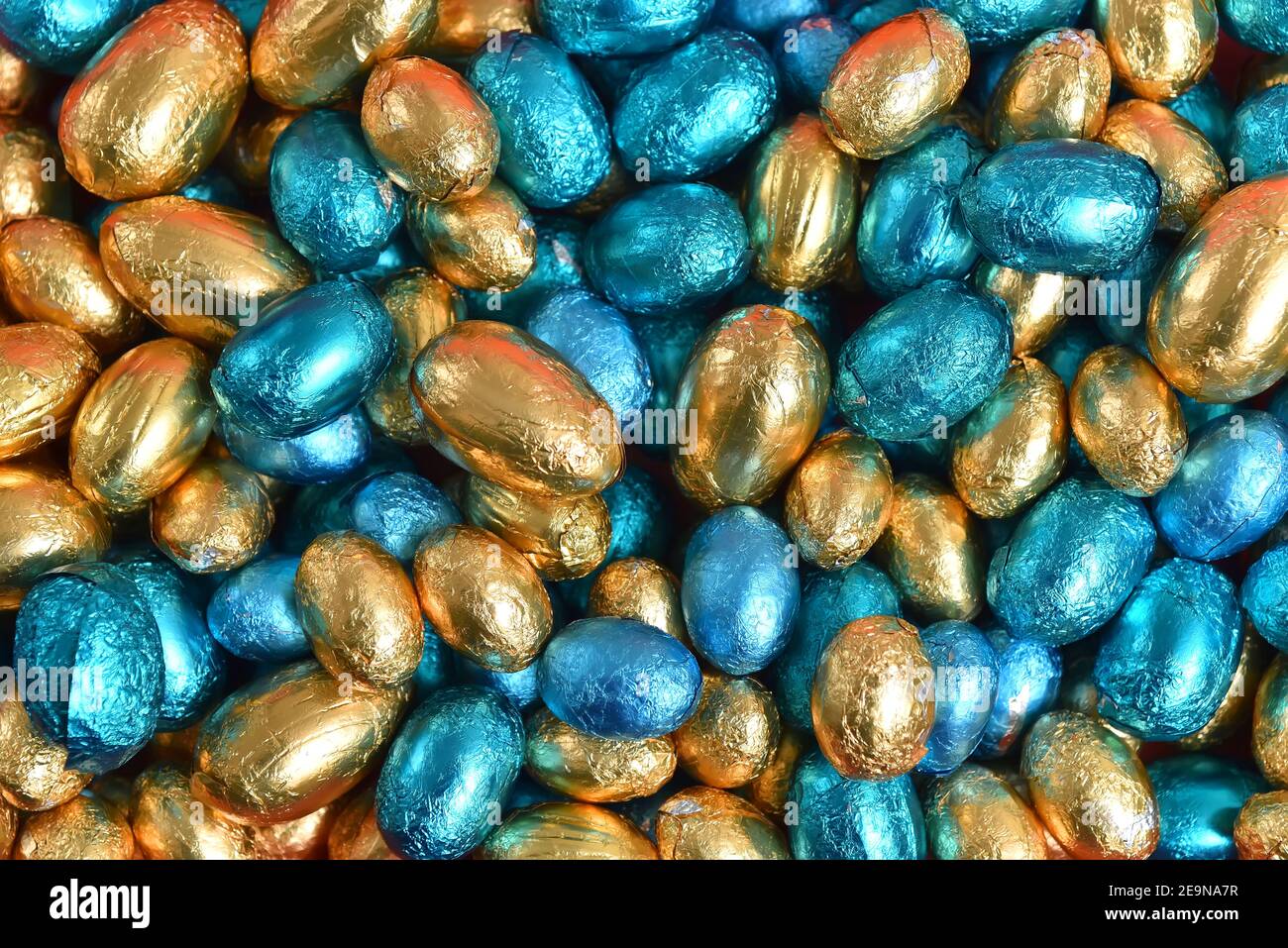 Blue,  gold and turquoise foil wrapped chocolate easter eggs, against a black background. Stock Photo