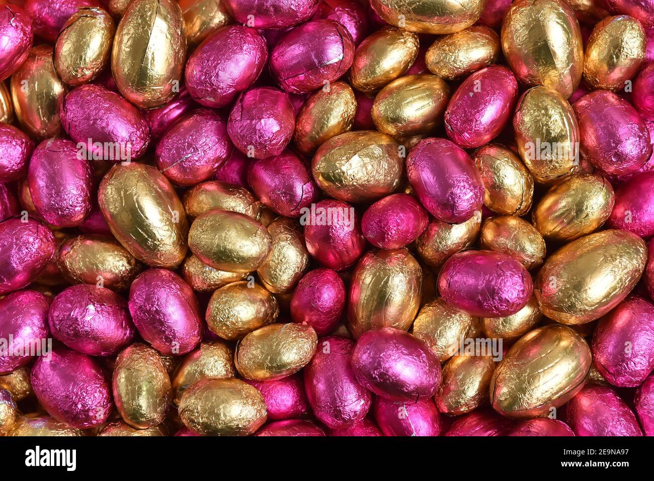 Large & small pink and gold foil wrapped chocolate easter eggs, against a peach orange background. Stock Photo