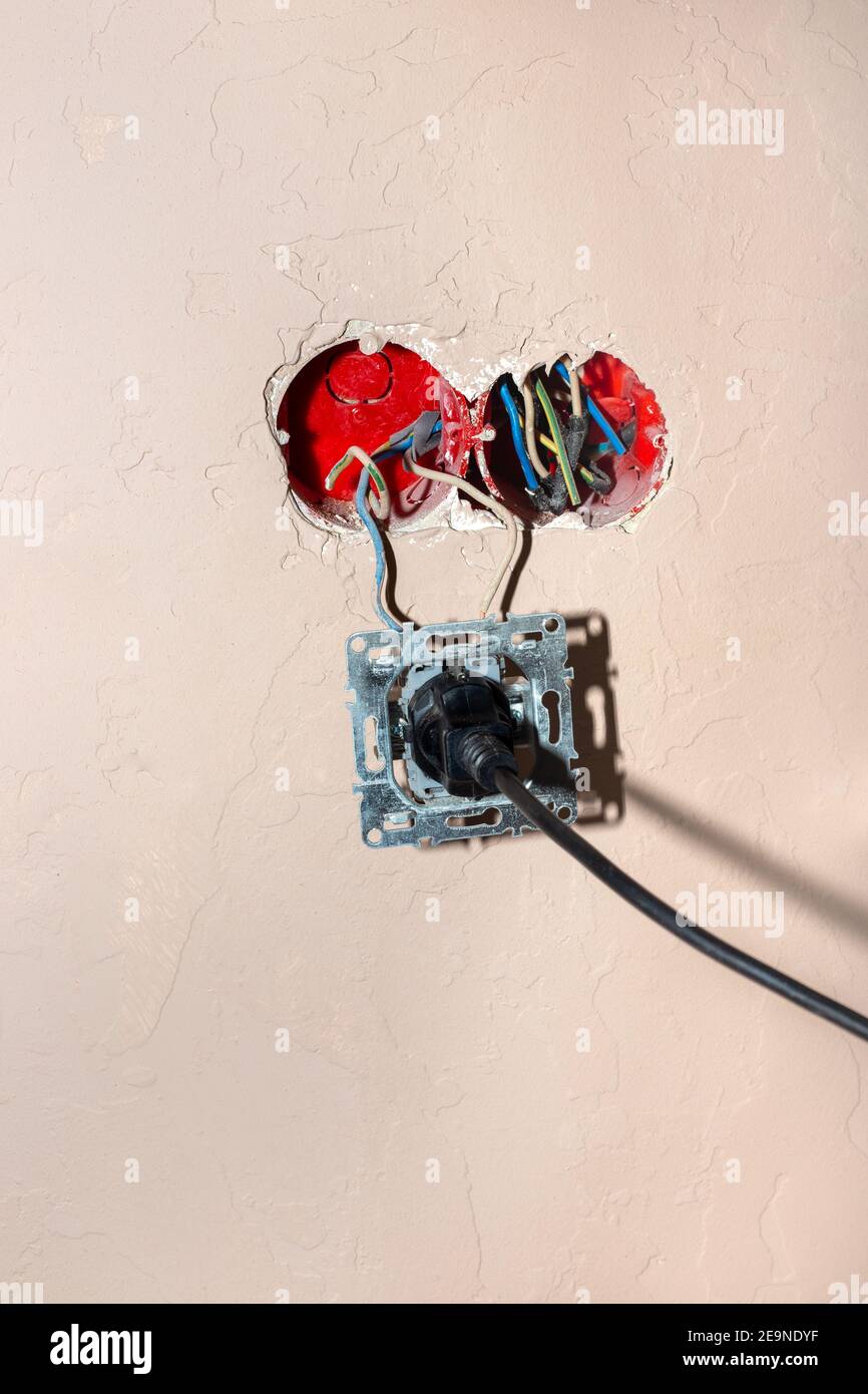 Broken electrical outlet with plug in. Danger of short circuit and fire. Improper use of devices. Stock Photo
