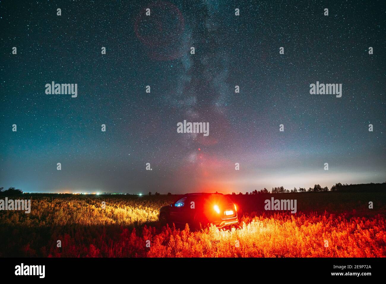 Milky Way Galaxy In Night Starry Sky With Glowing Stars Above Car SUV In Countryside Landscape. Milky Way Galaxy And Rural Field Meadow Stock Photo