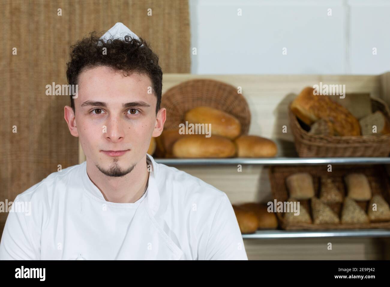 A tall and handsome baker in a baker's outfit stands behind the counter