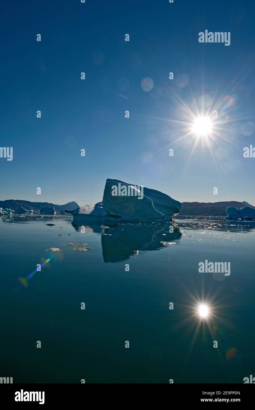 iceberg and sun reflecting in still fjord in South Greenland Stock Photo