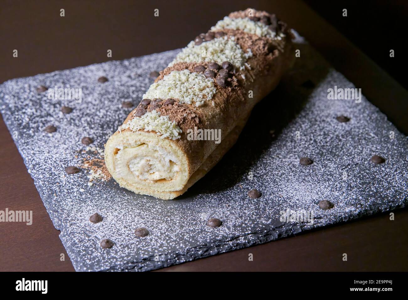Perspective view of a handmade gypsy arm of chocolate and cream with dark and white chocolate shavings on slate plate Stock Photo
