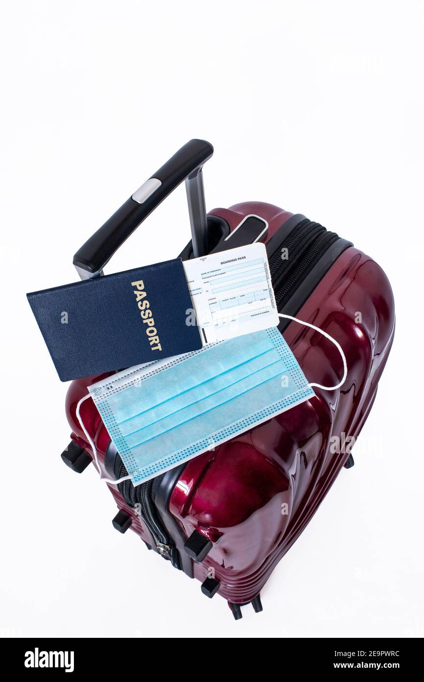 Travel suitcase, passport, boarding pass and medical mask isolated on white background. Concept of travel restrictions or ban during Covid-19 pandemic Stock Photo