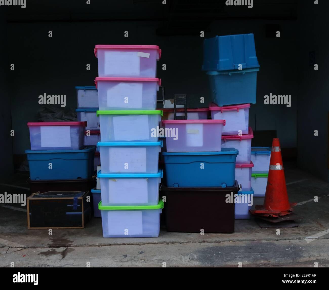 Stack of translucent plastic containers standing on cement floor in storage room, selective focus Stock Photo