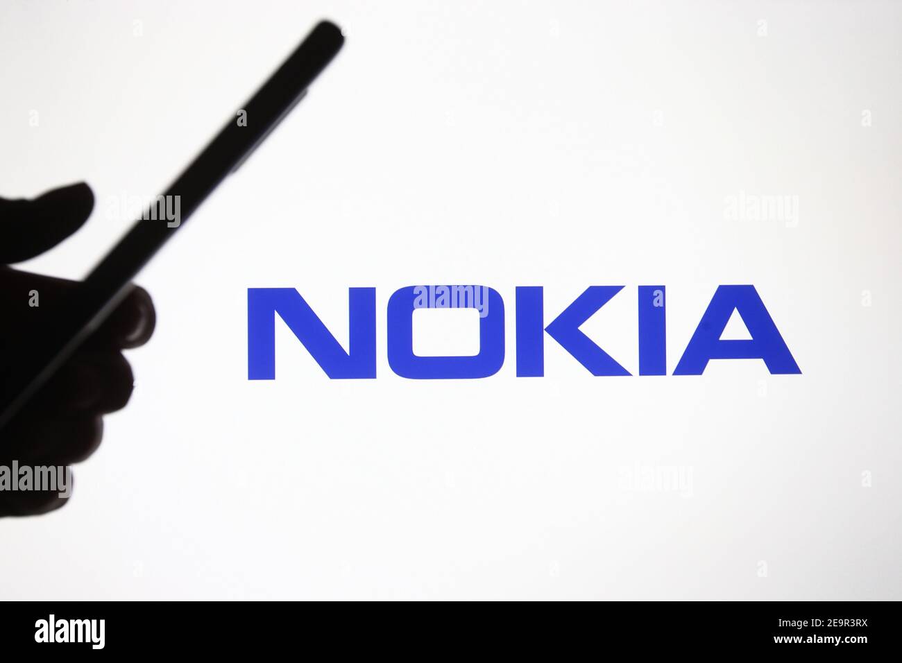 In this photo illustration a Nokia logo is seen in front of a silhouette hand holding a mobile phone. Stock Photo