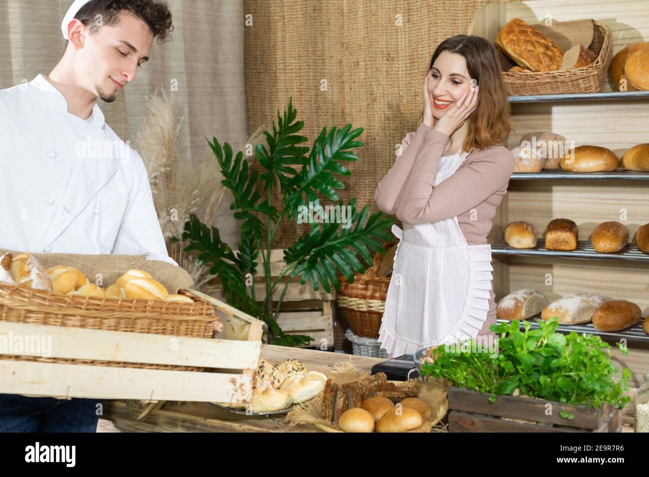 The new saleswoman was completely surprised by the delivery of bread brought by a handsome baker. A multi-generation baking tradition. Stock Photo