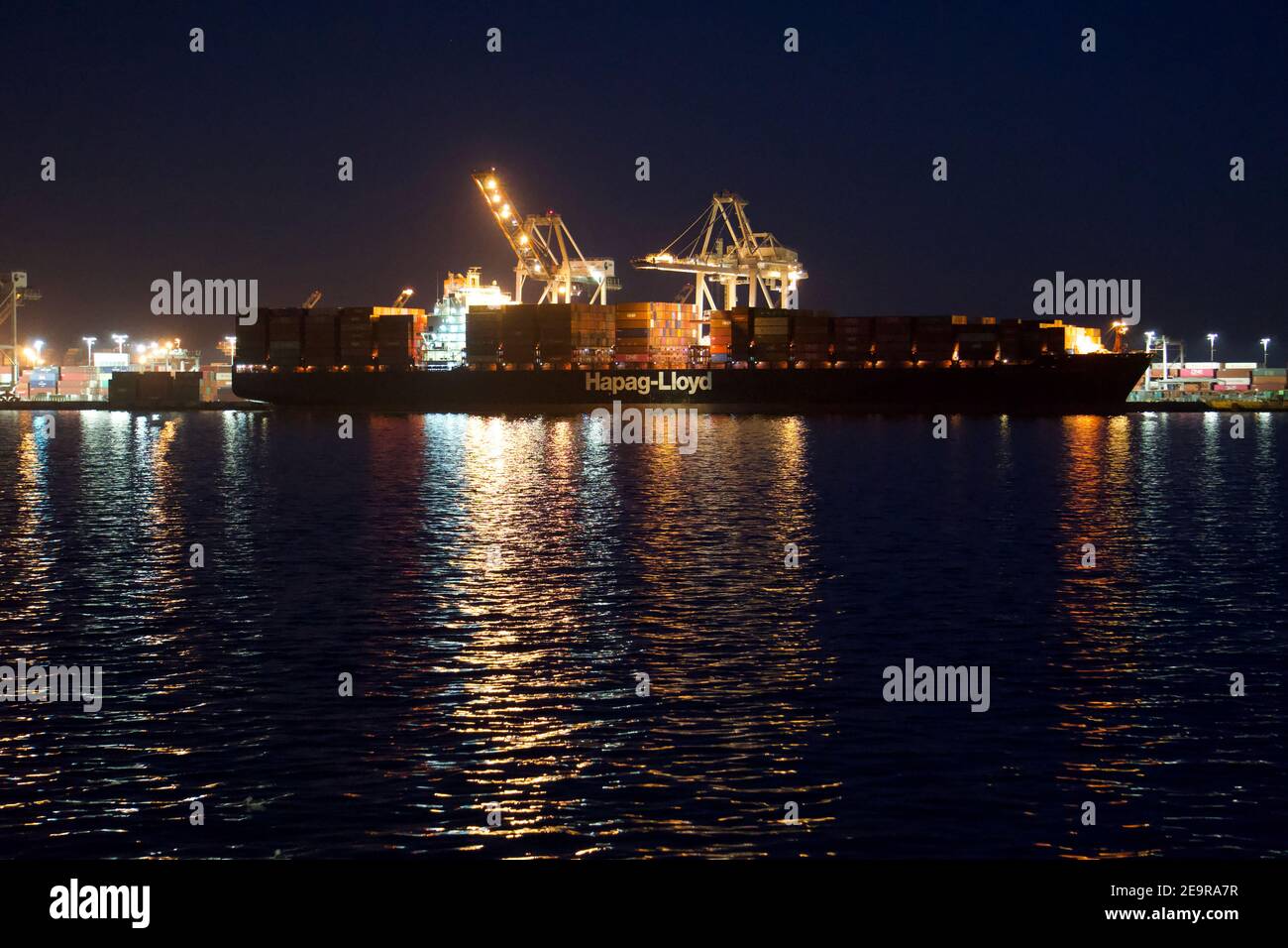 Hapag-Lloyd shipping container barge stacked with intermodal shipping containers with shipping cranes, at night. Port of Oakland, CA, USA Stock Photo