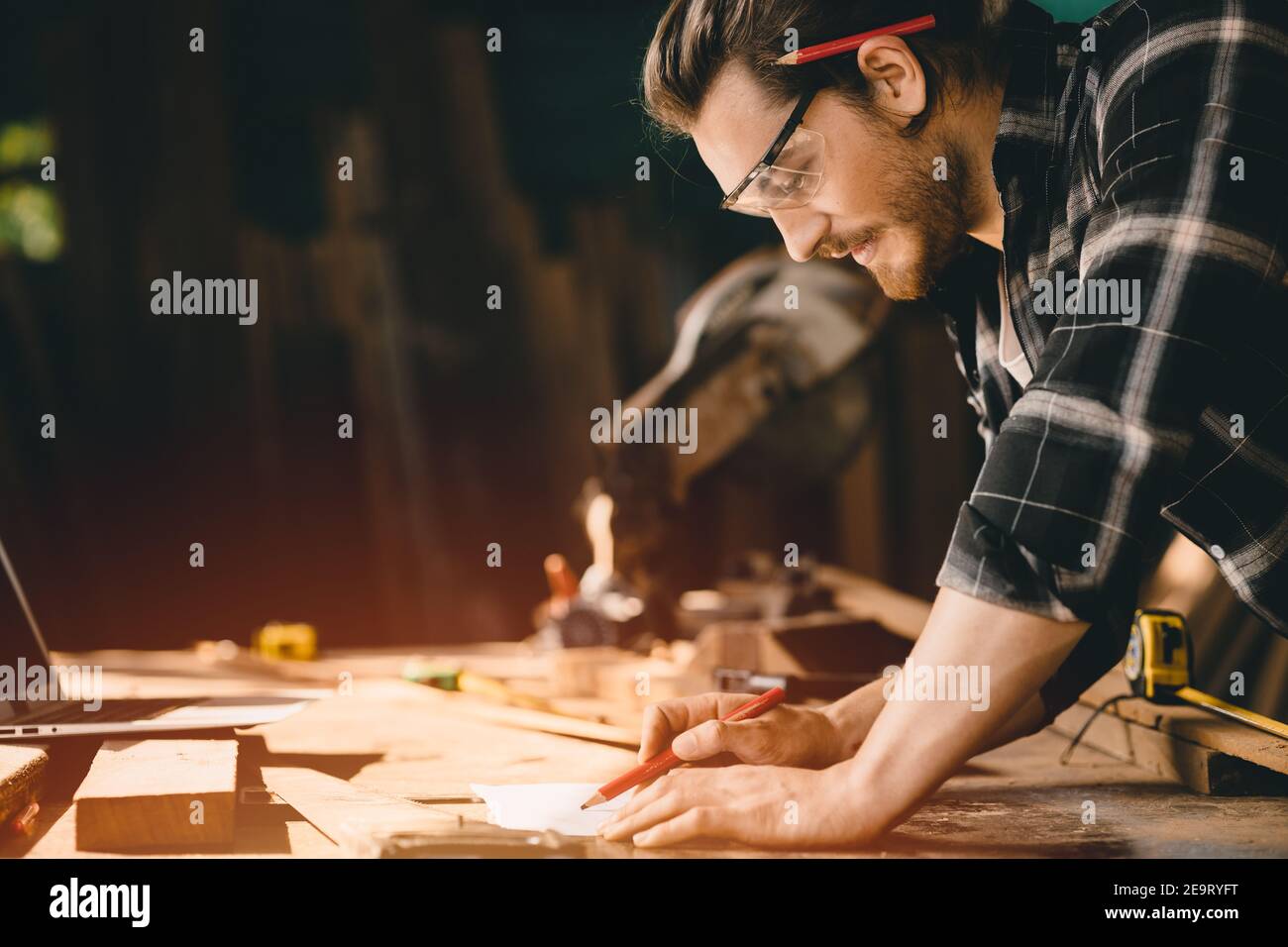 Happy Carpenter smiling to sketch design wooden furniture in wood workshop professional look high skill real authentic handcrafted working people. Stock Photo