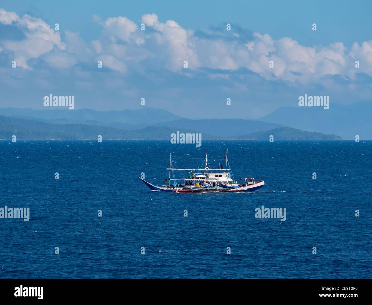 Traditional, wooden tuna fishing boat with outriggers at Sarangani Bay on its way to the fishing harbour in General Santos City, with the mountains of Stock Photo