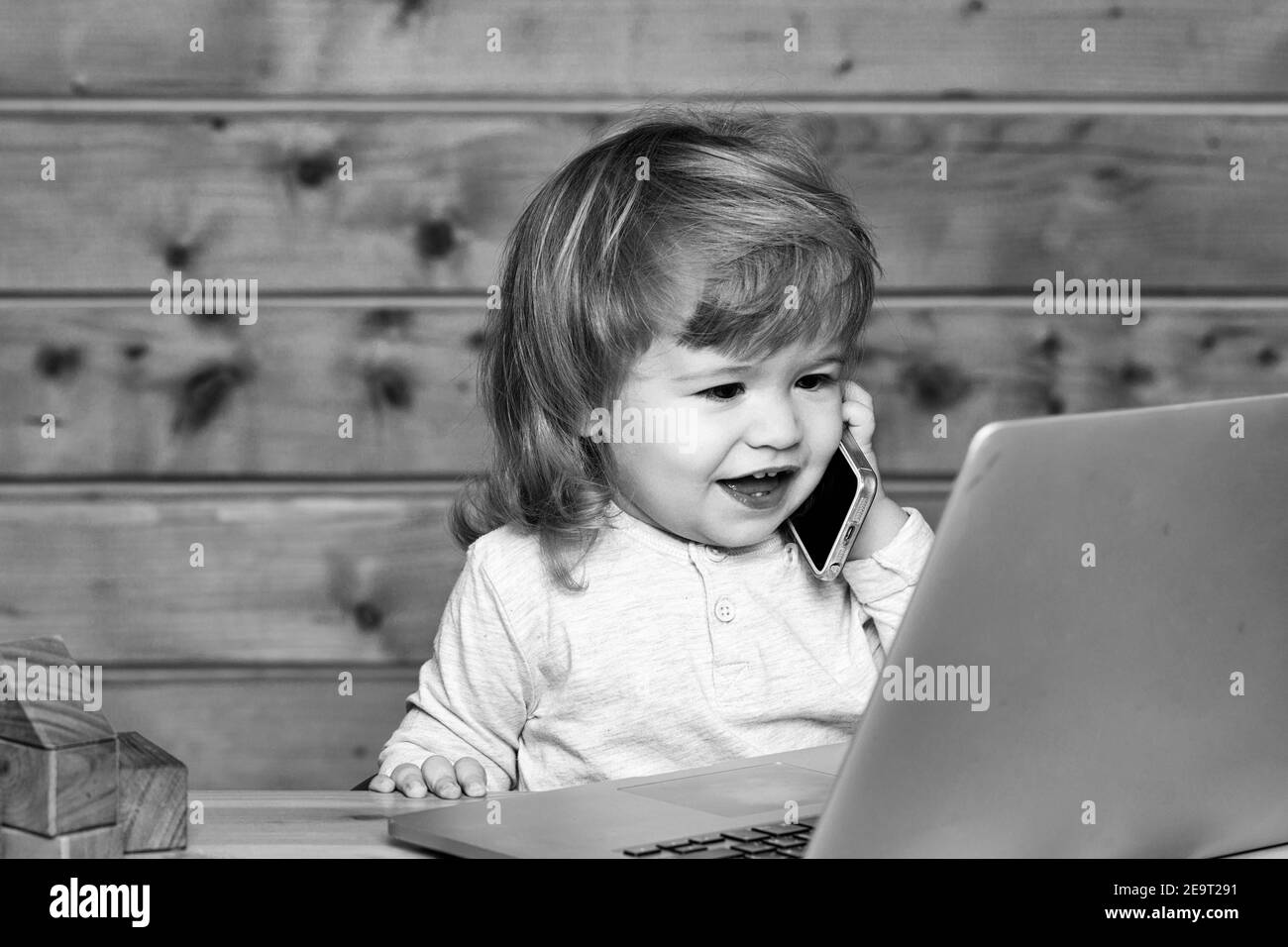 Happy baby boy child playing on notebook and mobile phone near toy building blocks indoors. Stock Photo