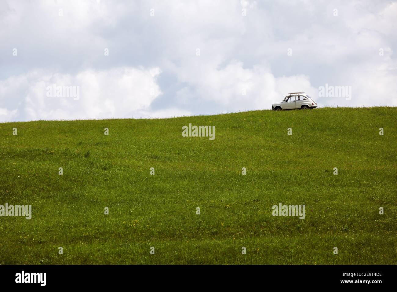An old white car in the middle of a green unmown meadow with a cloudy sky in the background. Stock Photo