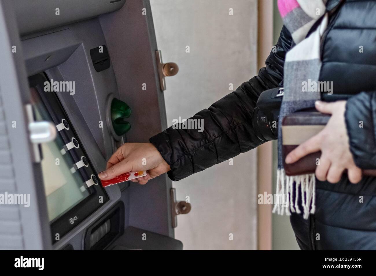 Female hands hold a plastic bank credit card, use an ATM machine to