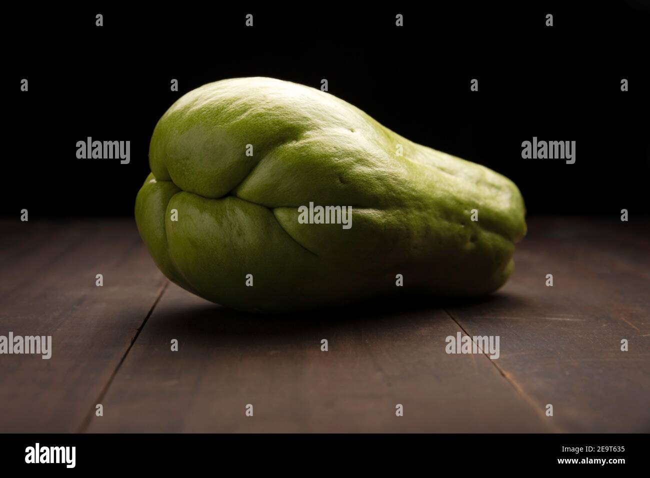 image of a chayote fruit close up on rustic wooden surface and black background Stock Photo