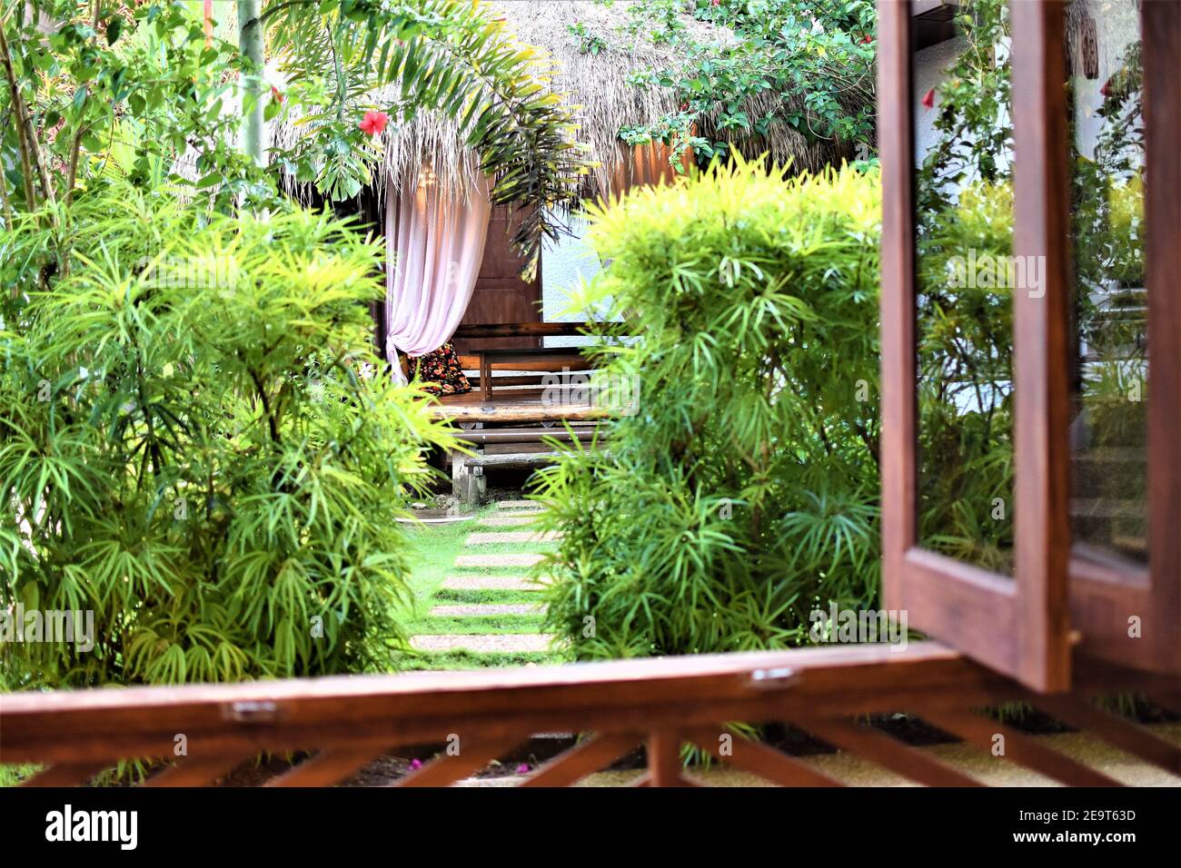 A curtained bamboo garden cabana with a nipa roof can be seen from an open house window Stock Photo