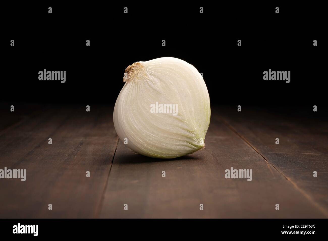 image of a half an onion close up on rustic wooden surface and black background Stock Photo