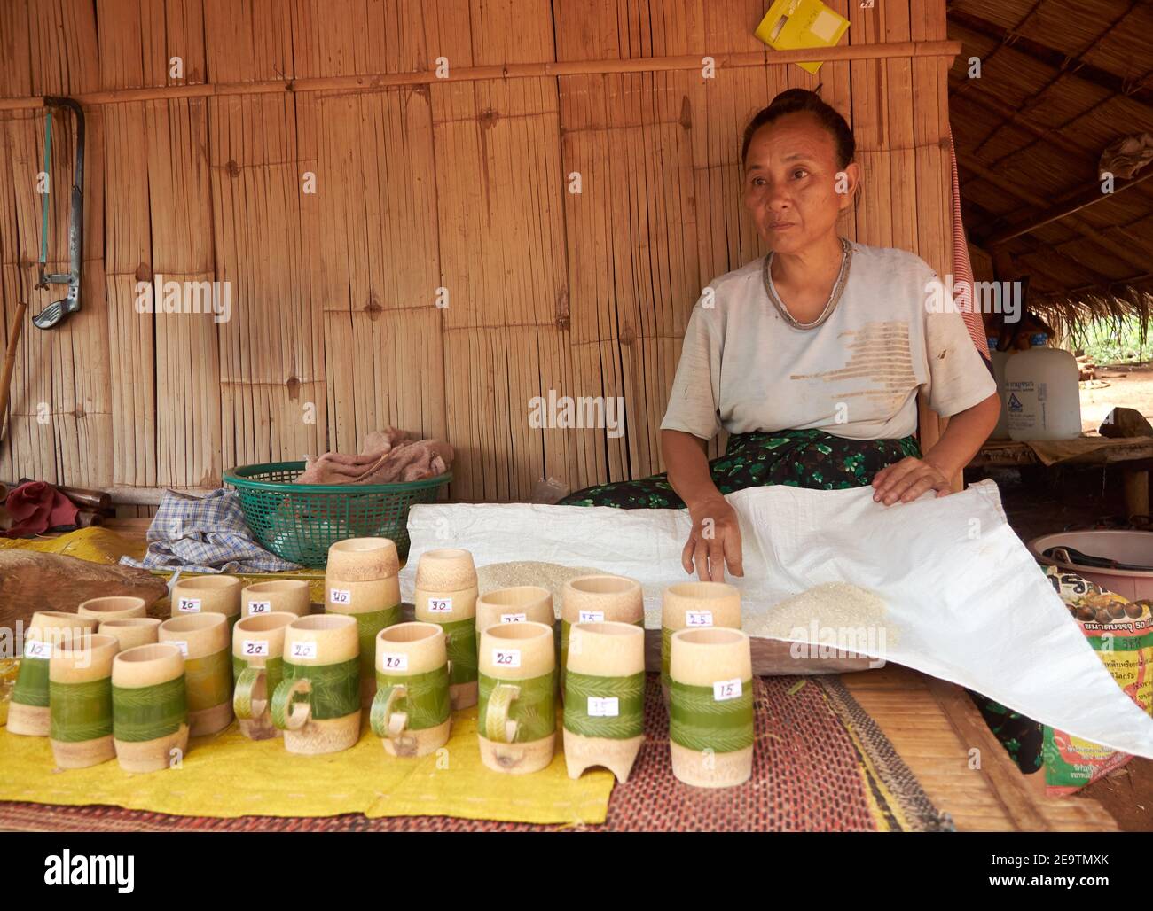 A woman is checking her rice while waiting for the buyer of her merchandise in the form of bamboo mug Stock Photo