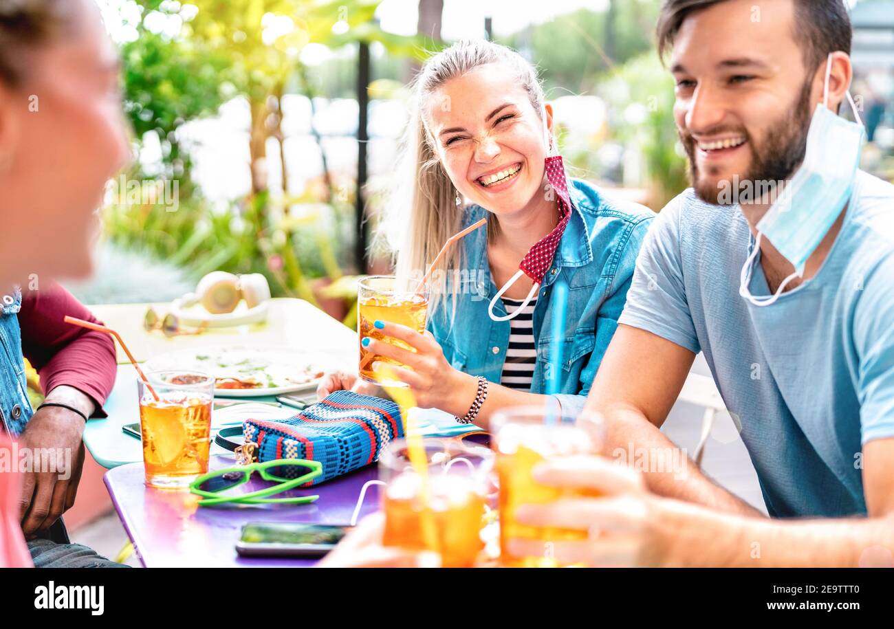 Friends drinking at cocktail bar with opened face masks - New normal friendship concept with people having fun together toasting drinks Stock Photo