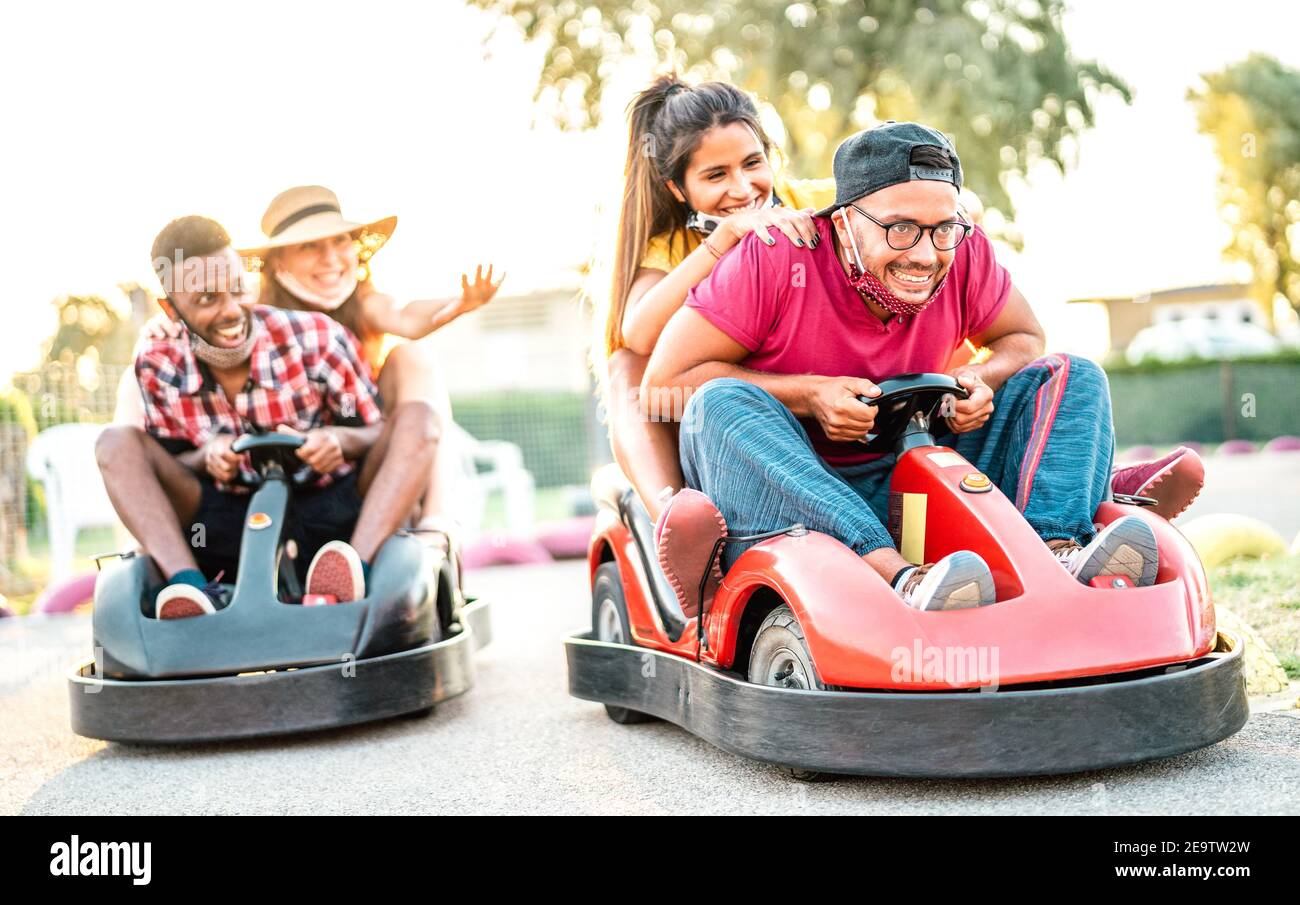 Milenial friends having fun at children playground on go kart race - Young people with face mask competing on mini car racing - New normal lifestyle Stock Photo