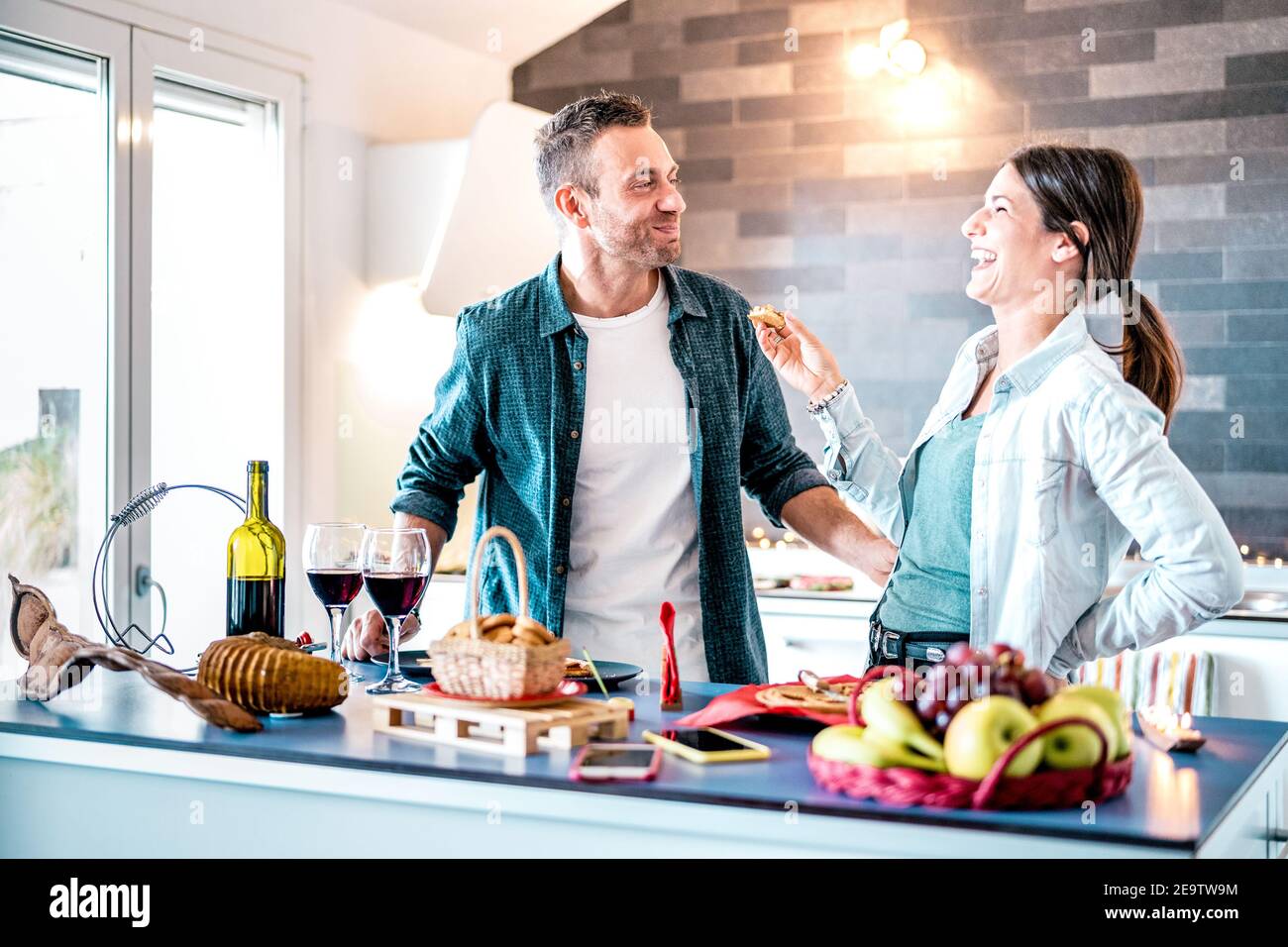 Young couple in love having fun at house kitchen - Happy millenial lovers enjoying lunch together at home on jubilee anniversary Stock Photo