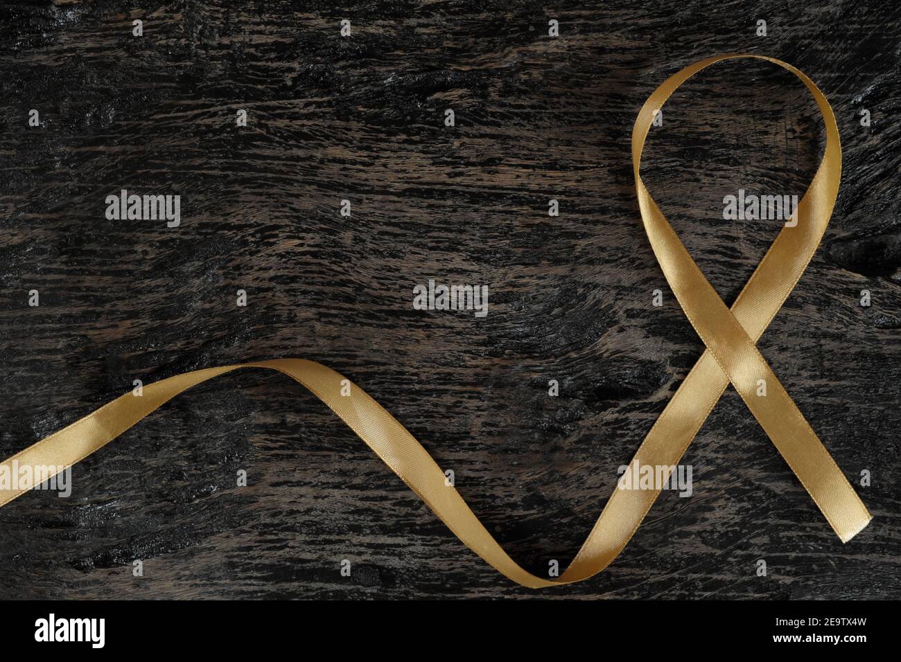 Top view of gold ribbon on dark wood background. Childhood cancer awareness concept. Stock Photo