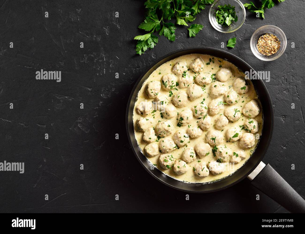 Delicious homemade swedish meatballs with creamy white sauce in frying pan over black stone background with free space. Top view, flat lay, close up Stock Photo
