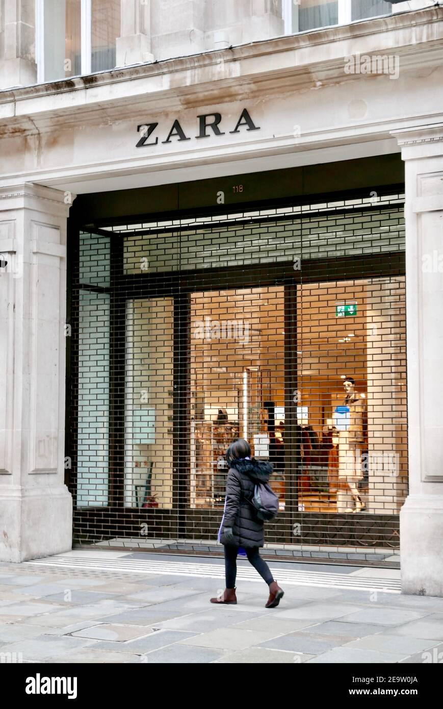 A young woman walks past Zara clothes shop currently closed due to covid19 pandemic lockdown which is impacting the economy. Regent Street, London, UK Stock Photo