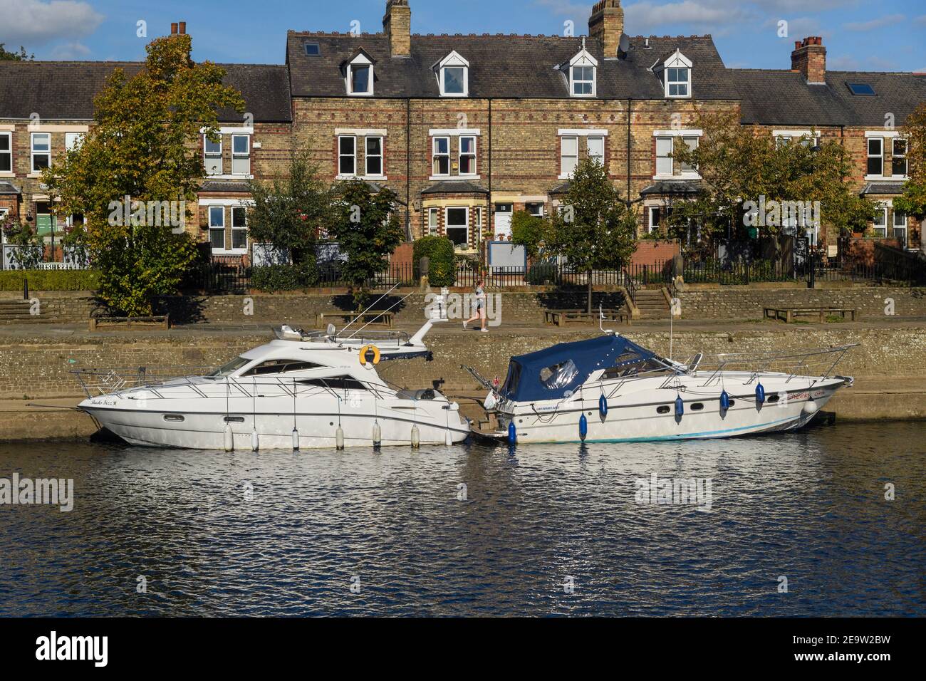 River Ouse in York - boats (leisure cruisers) moored at quayside by row of houses (terrace) & jogger on riverside path - North Yorkshire, England, UK. Stock Photo