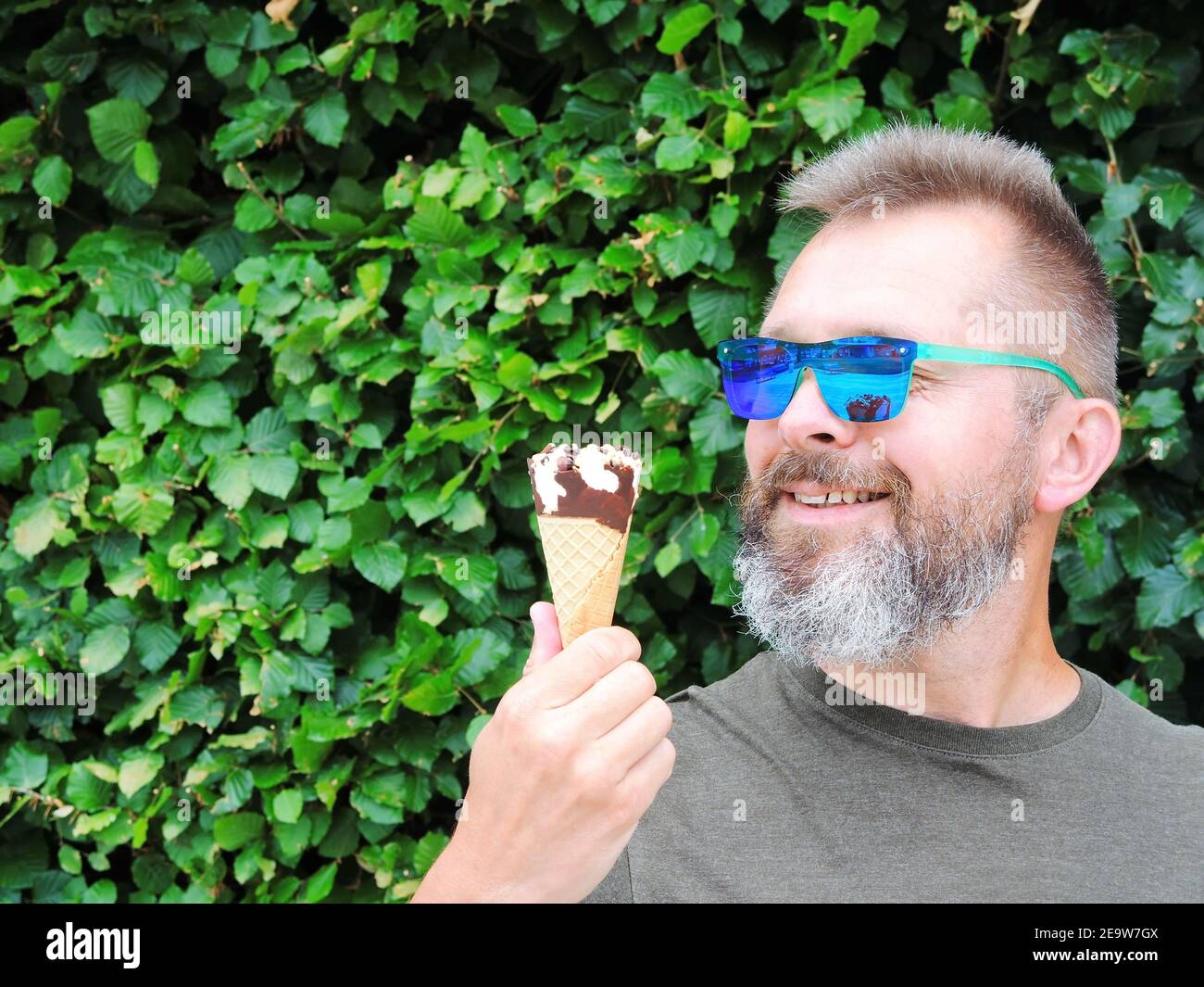 A handsome bearded man in sunglasses holds an ice cream cone in his hands and smiles Stock Photo