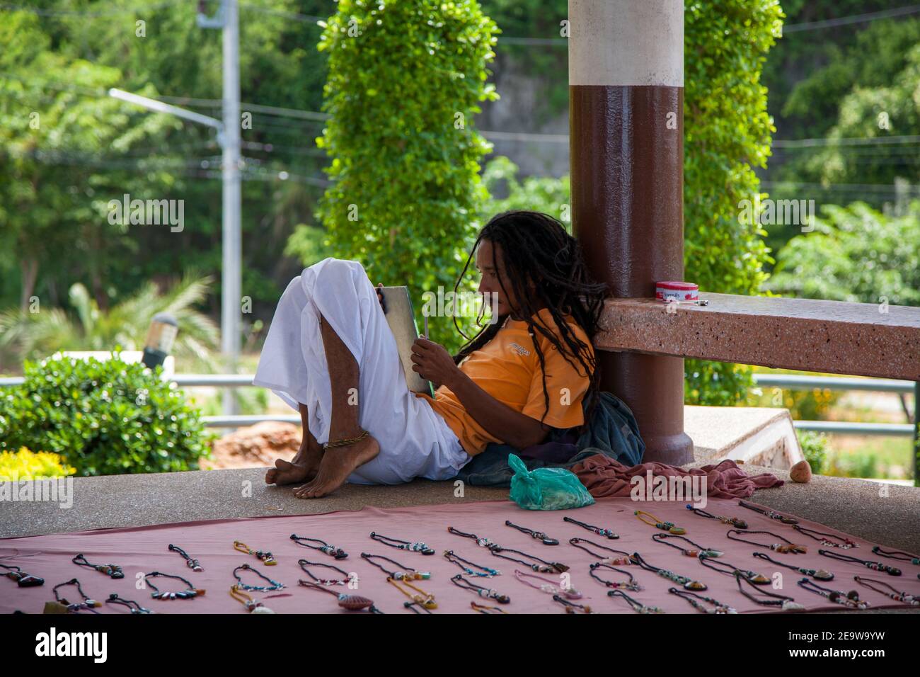 Man with dreadlocks reading whilst selling handmade jewellery in Krabi, Thailand, South East Asia. Stock Photo