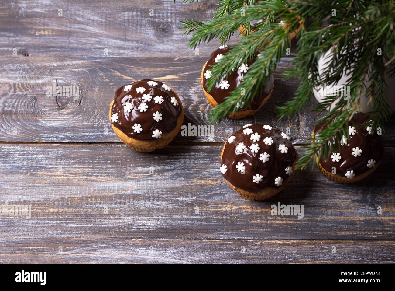 Spicy pumpkin muffins with nuts, decorated with chocolate glaze and sugar snowflakes under the Christmas tree on a wooden table, free space, selective Stock Photo