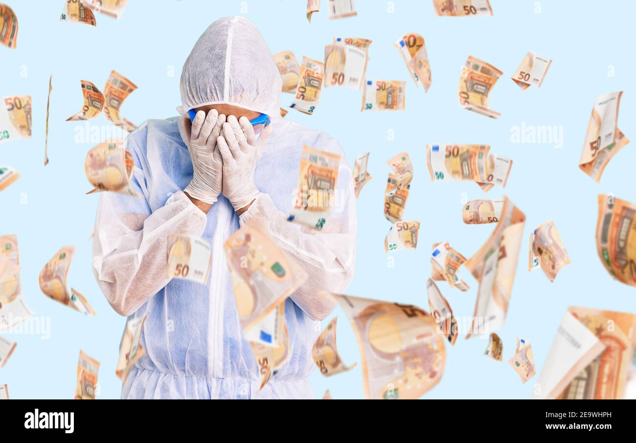 Young hispanic man wearing doctor protection coronavirus uniform and medical mask with sad expression covering face with hands while crying. depressio Stock Photo