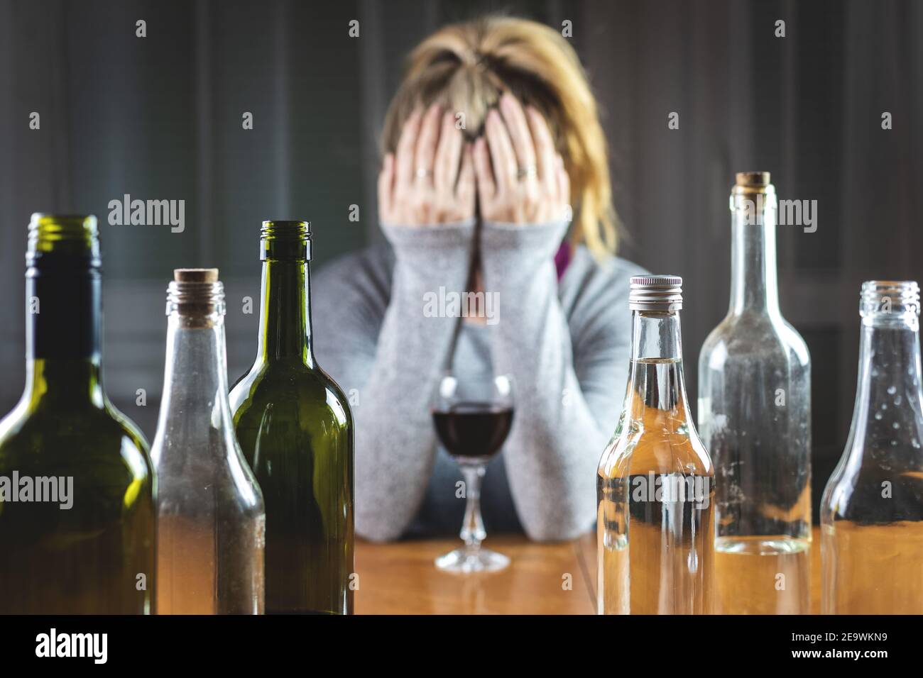 Alcoholism concept with woman and bottles indoors. Real people with alcohol abuse problem. Selective focus on bottles Stock Photo